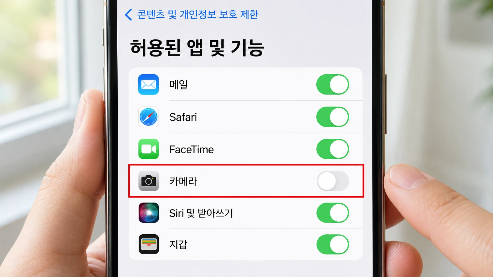 손에 든 아이폰의 허용된 앱 및 기능 화면에서 카메라 토글을 누르려는 엄지손가락